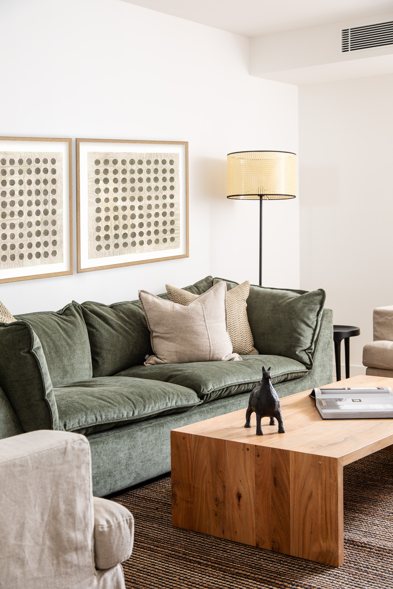 A living room with a green sofa, neutral pillows, a wooden coffee table with decor, a floor lamp, and abstract art on the white wall—perfect Airbnb Furnishing for a stylish and inviting space.